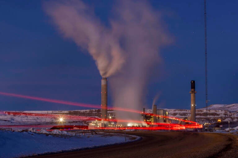 Smoke rises from a power plant, as the lights glow red in a snowy landscape at night.