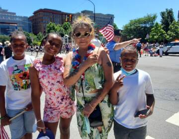 A group of people stand on the side of the street, holding the American flag and smiling.