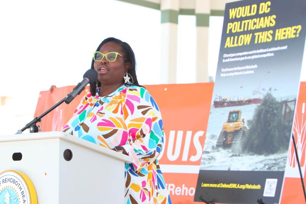 Roishetta Ozane speaks at a podium, with a sign behind her.