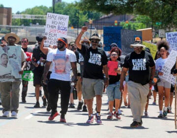 A group of people walks, carrying signs protesting the police shooting and death of Jayland Walker.