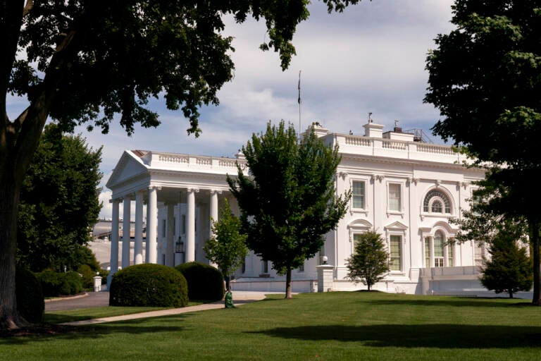 The White House is seen from afar, surrounded by trees.