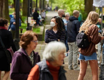 People walk on a sidewalk, masked.
