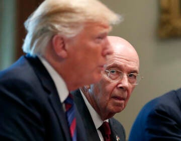 President Donald Trump is seen in the foreground, as Commerce Secretary Wilbur Ross listens in the background