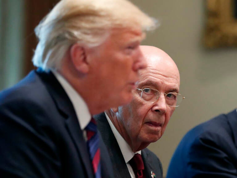 President Donald Trump is seen in the foreground, as Commerce Secretary Wilbur Ross listens in the background