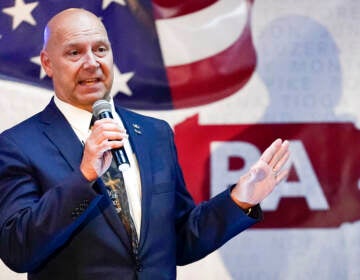 Doug Mastriano speaks in front of an image of the American flag and PA written in the background.