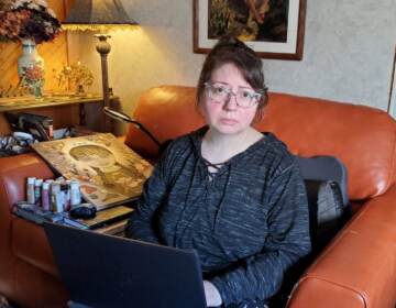 A woman sits in an armchair with a laptop in front of her.