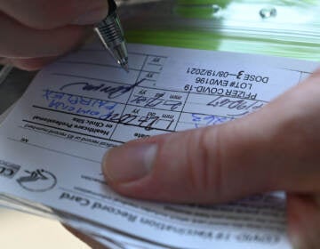 A nurse marks a COVID vaccine card with information about a booster dose