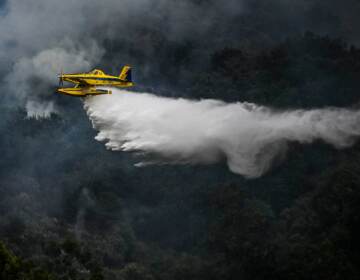 A helicopter sprays water, as forests are visible below.