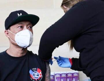 A person wearing a face masks looks forward as a healthcare professional gives them a vaccine in their arm.