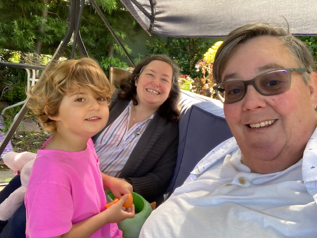 A selfie of Beth Kenny (foreground), their wife Adina (middle), and their child Vyla sitting in their backyard