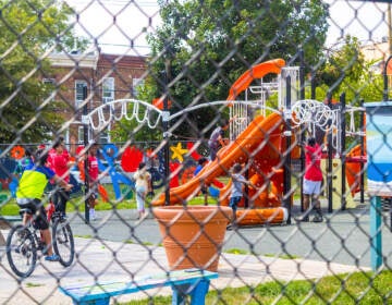 Kids play on a playground as seen through a fence in the foreground.