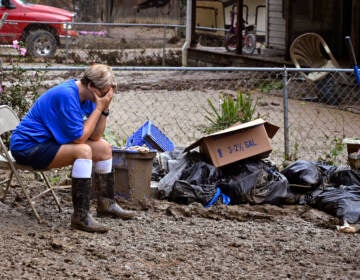 A woman sits with her head in her hands next to a pile of debris.