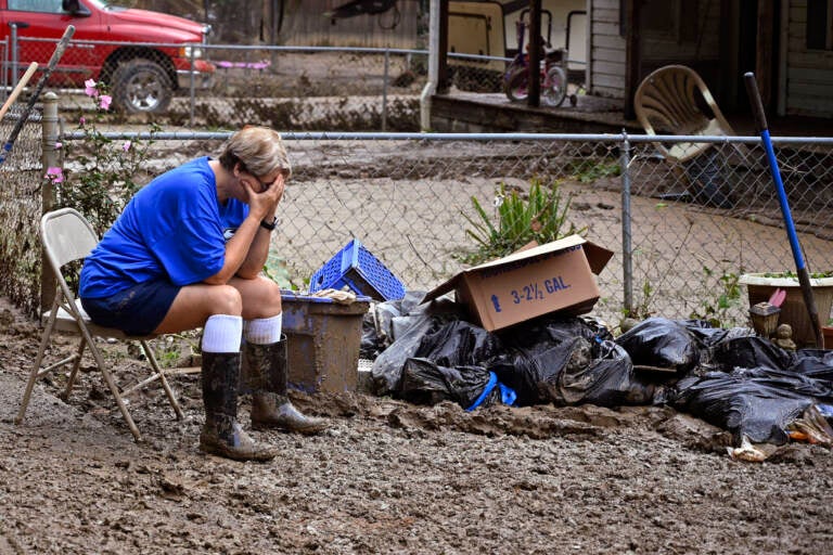 A woman sits with her head in her hands next to a pile of debris.