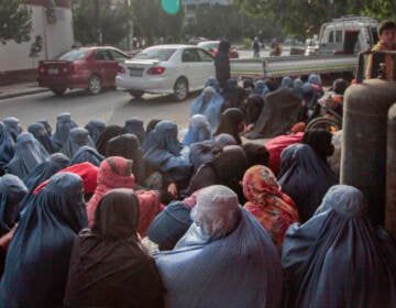 A group of women in burqas are sitting outside of a bakery.