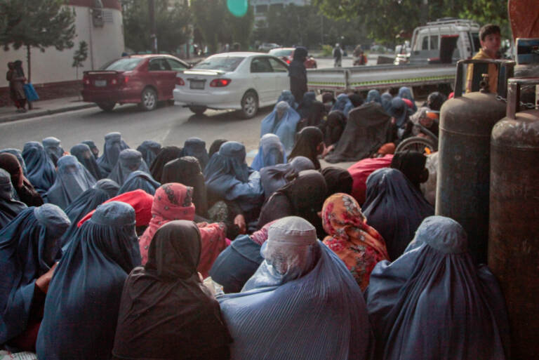 A group of women in burqas are sitting outside of a bakery.