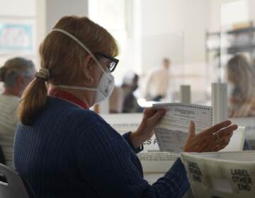 An election worker processes mail ballots while wearing a face mask.