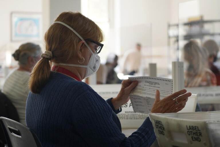 An election worker processes mail ballots while wearing a face mask.