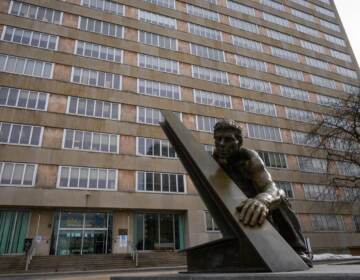 A statue of someone holding up something is visible in front of a tall building.