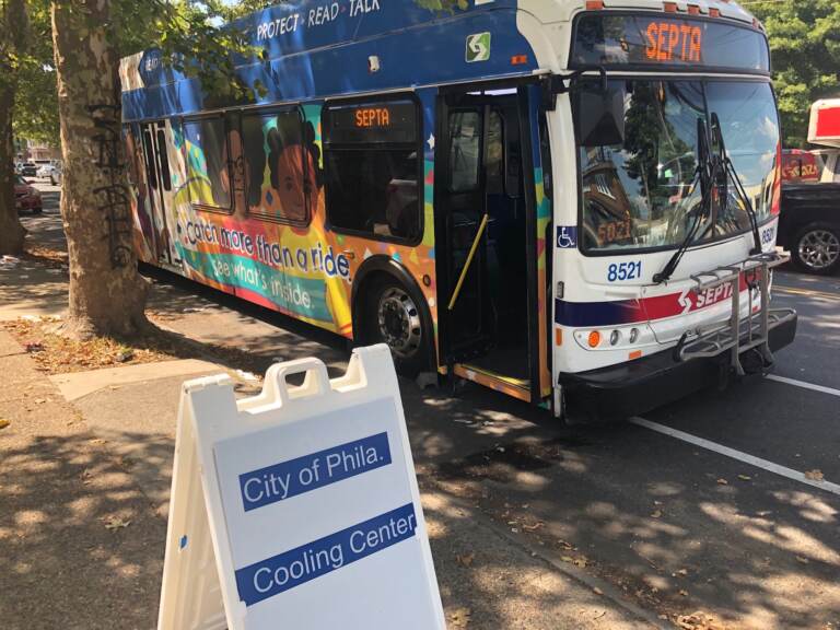 A bus that reads SEPTA on the front is parked by the curb. In front of it is a sign that advertises that it's a cooling center.