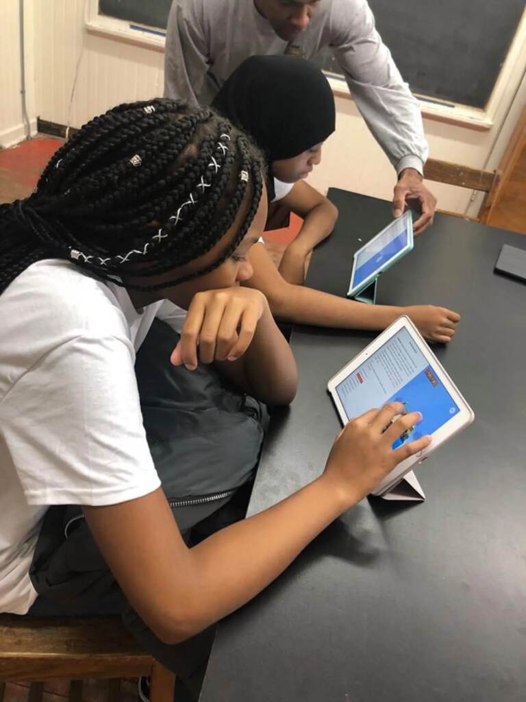 Several girls peer closely at a tablet.