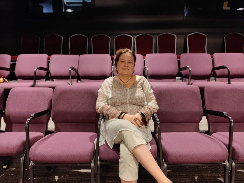 Che'Rae Adams is in the center of the photo, smiling, sitting in the audience seats of the Drake Theatre.