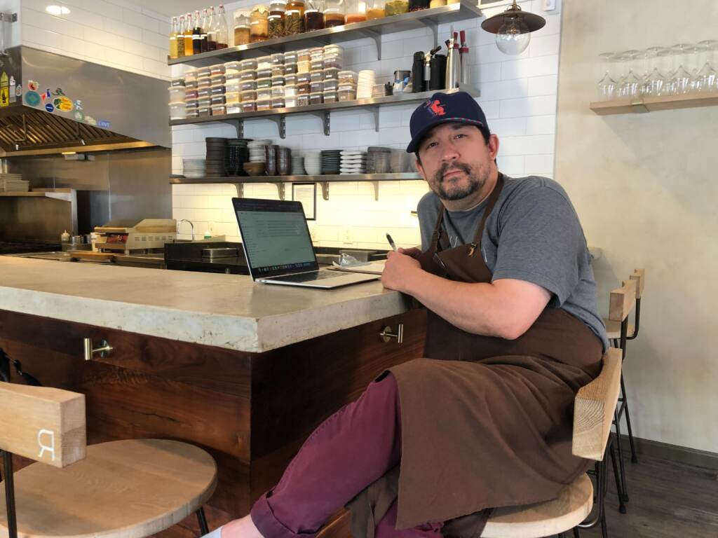 Randy Rucker leans at a bar, facing the camera, his laptop open in front of him.