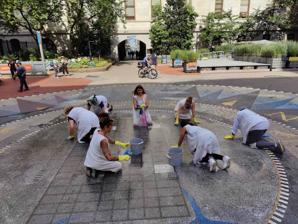 A view from above of a group of people scrubbing the floor in the middle of City Hall's central plaza as onlookers watch.