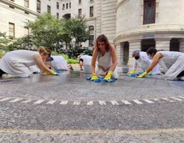 Women in white smocks wipe the ground in the center of Philadelphia's City Hall.