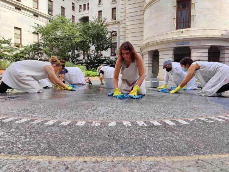 Women in white smocks wipe the ground in the center of Philadelphia's City Hall.