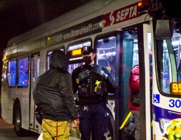 A police officer stands at the doorway of a bus as someone goes to get on.