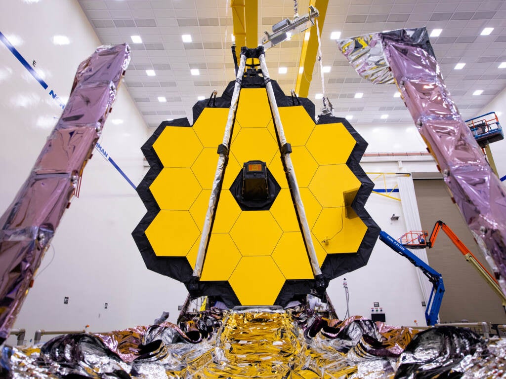 An image of the James Webb Space Telescope, a tall circular yellow device, being tested on earth.