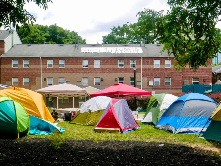 Tents are visible on a lawn in front of a red-brick building.