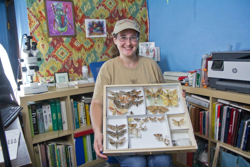 Trisha Nichols smiles as she holds a display case of insects.