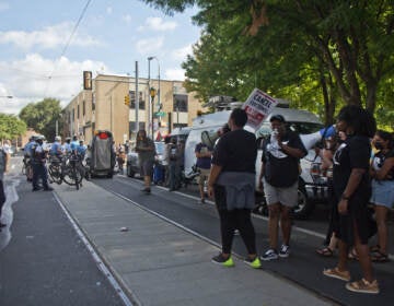 A crowd gathers on a sidewalk in front of an apartment building.