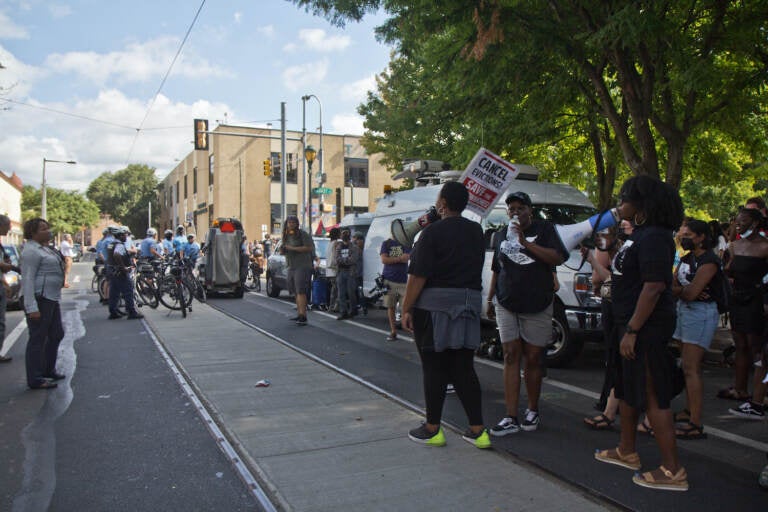 A crowd gathers on a sidewalk in front of an apartment building.