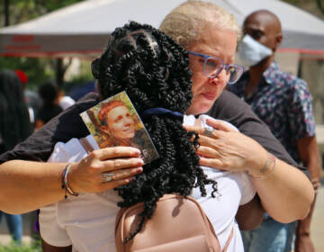 Terri Spina shares a tearful hug at the opening ceremony of the Philadelphia Overdose Memorial Garden at Thomas Paine Plaza in 2022. Spina holds a photo of her daughter, Ginamarie Vicent, who died of an overdose at the age of 31. (Emma Lee/WHYY)