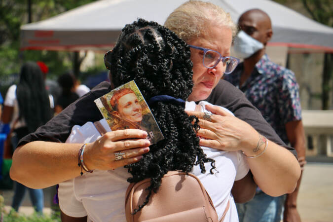 Terri Spina shares a tearful hug at the opening ceremony of the Philadelphia Overdose Memorial Garden at Thomas Paine Plaza. Spina holds a photo of her daughter, Ginamarie Vicent, who died of an overdose last year at the age of 31. (Emma Lee/WHYY)