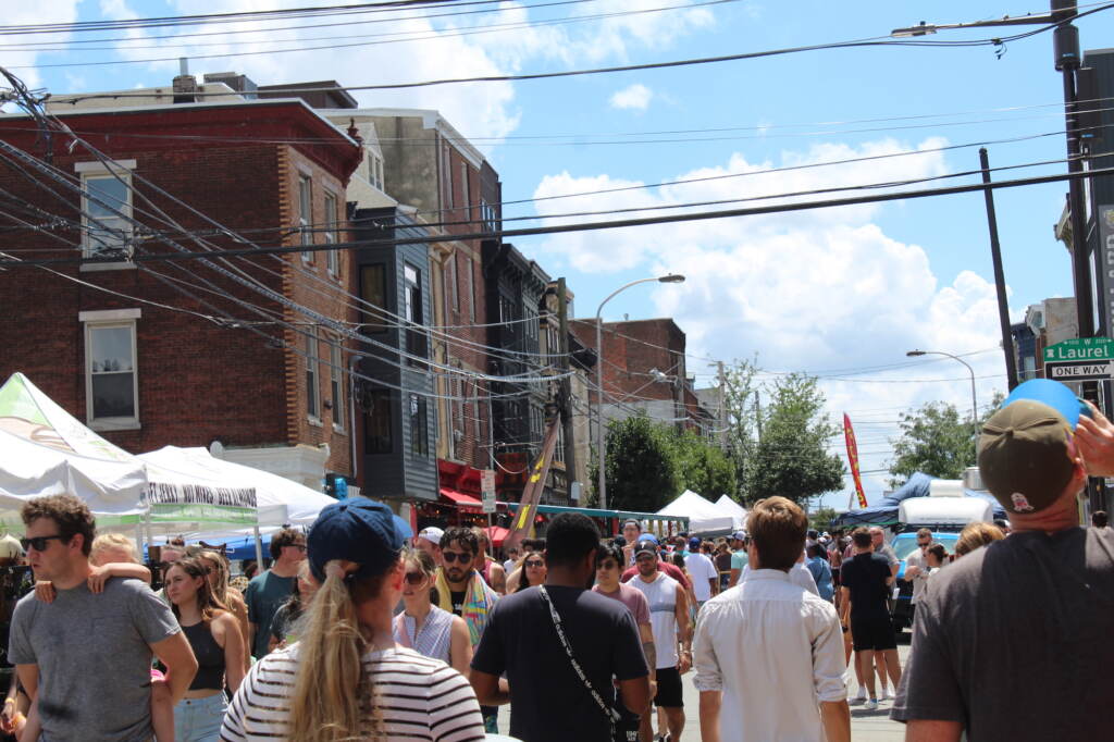 A crowd walks down a street. Buildings are visible in the background.