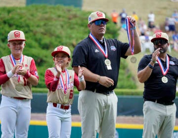 Jace Oliverson, center, father of Little Leaguer Easton Oliverson who was injured, holds Easton's medal, with another son, Brogan Oliverson (6) at his side, taking Easton's place on the championship team from Santa Clara, Utah before a baseball game against Nolensville, Tenn., at the Little League World Series in South Williamsport, Pa., Friday, Aug. 19, 2022. (AP Photo/Gene J. Puskar)