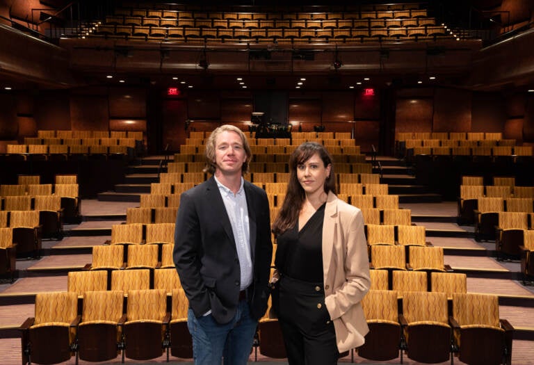 Tyler Dobrowsky and wife Taibi Magar pose with audience theater seats visible behind them.