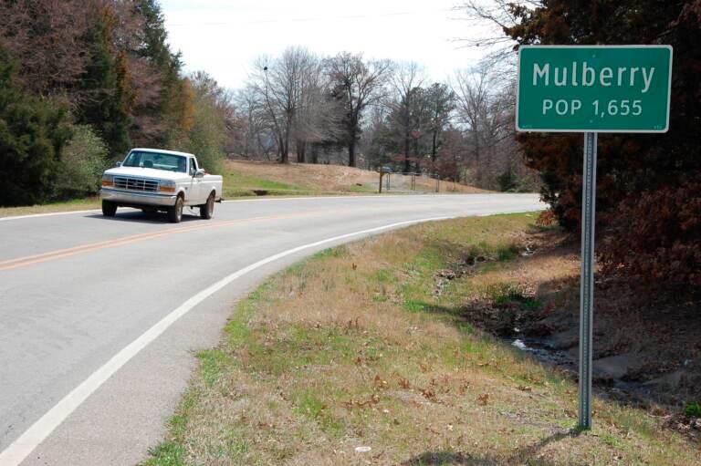 A truck drives near a population sign in Mulberry, Arkansas