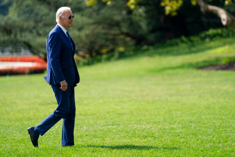 President Joe Biden walks across a green lawn.