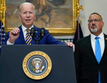 President Joe Biden speaks about student loan debt forgiveness in the Roosevelt Room of the White House. Education Secretary Miguel Cardona listens at right.