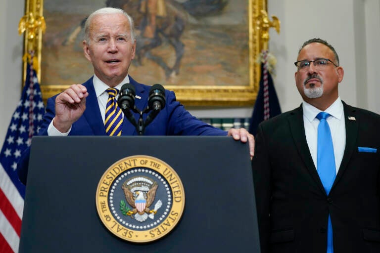 President Joe Biden speaks about student loan debt forgiveness in the Roosevelt Room of the White House. Education Secretary Miguel Cardona listens at right.