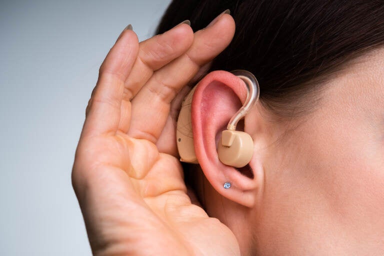 Close-up Of A Woman's Hand Inserting Hearing Aid In Her Ear