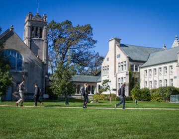 Students walk across grass on a green campus with buildings in the background.