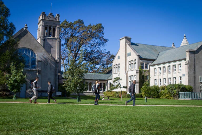 Students walk across grass on a green campus with buildings in the background.