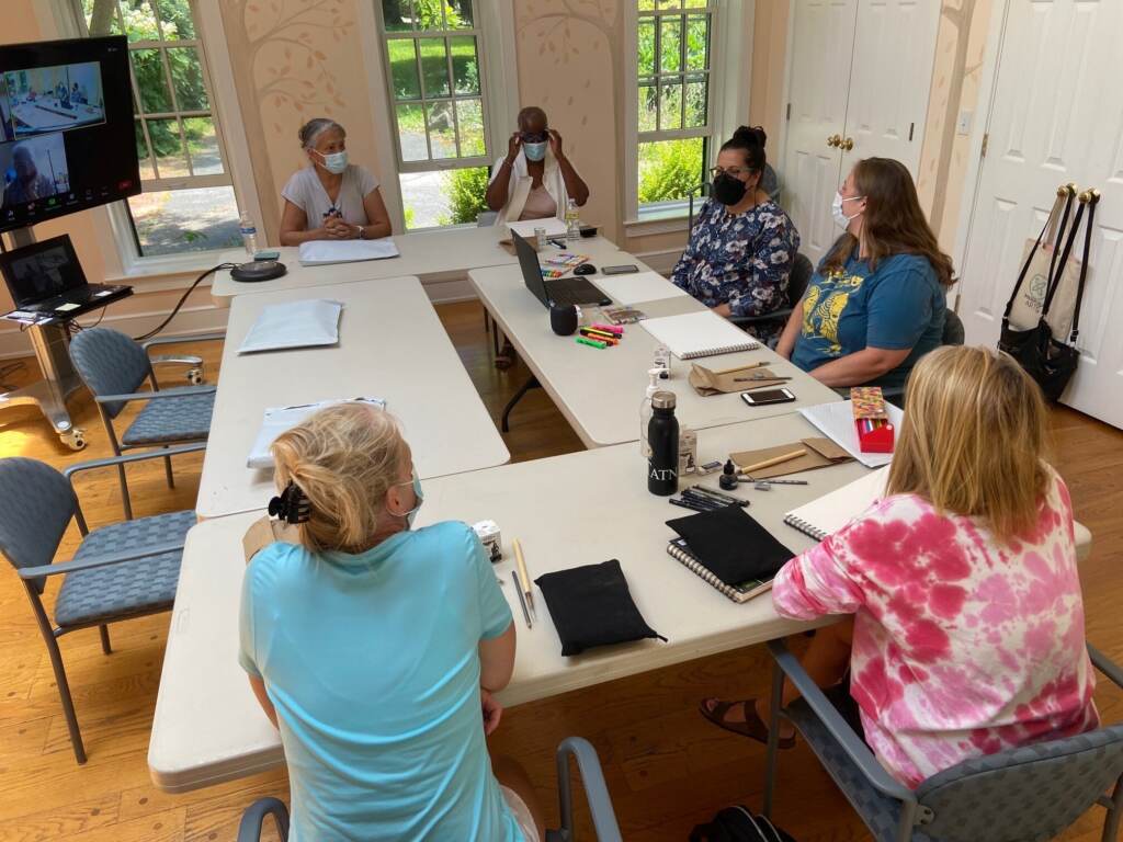 A group of people are seated, gathered around a rectangular table. Photo view is from above.