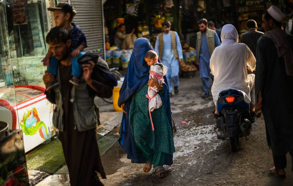 A woman wearing a traditional burqa and carrying a child walks through a market in Kabul