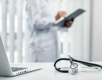 A doctor is standing and reading a report as a stethoscope is seen on a table